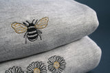 Close up of embroidered bumble bee on a grey sweatshirt. Stacked on a daisy sweatshirt, also available on our online store.