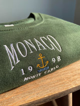 Close up detailed embroidered Monaco design, photographed on forest green sweatshirt.