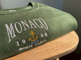 Close up detailed embroidered Monaco design, photographed on forest green sweatshirt.