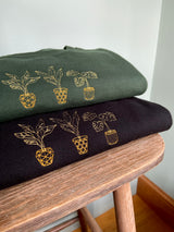 Embroidered golden house plant design, stack of two sweatshirts on forest green and black.