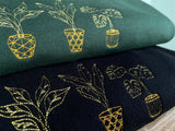 Close up of embroidered golden house plant design, stack of two sweatshirts on forest green and black.