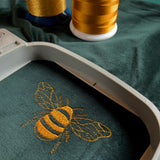 Close up shot of the golden embroidered bee on the velvet Forest Green zip cushion cover. Within an embroidery hoop.