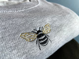 Close up of embroidered bumble bee on a grey sweatshirt.