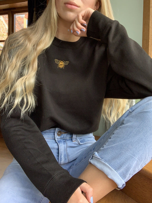 Embroidered golden bumble bee design modelled on a black sweatshirt. Styled with high waisted jeans.