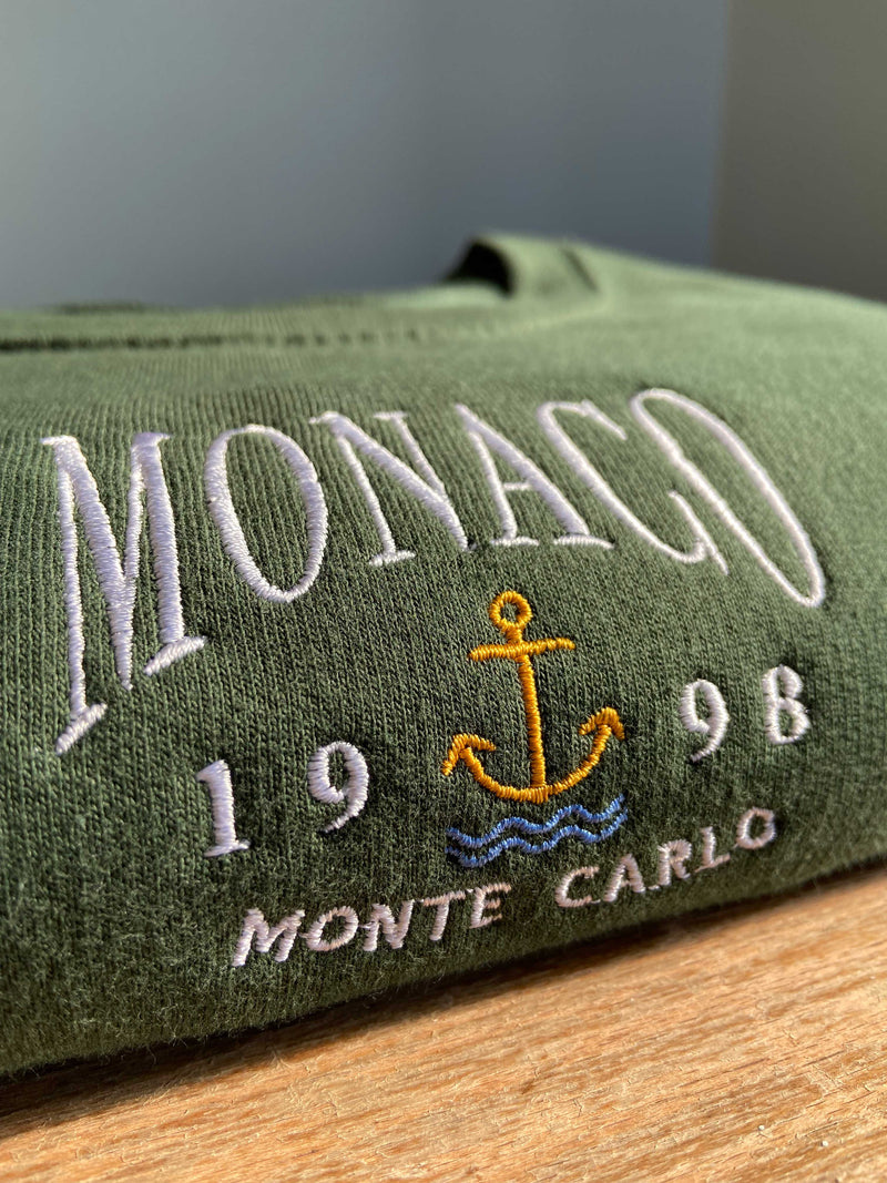Close up detailed embroidered Monaco design, photographed on forest green sweatshirt.