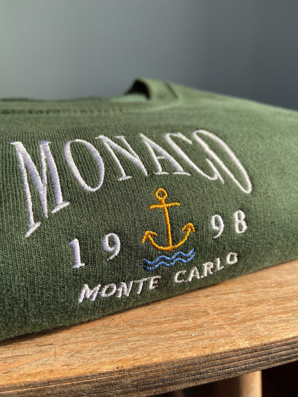 Close up detailed embroidered Monaco design, photographed on forest green sweatshirt. 