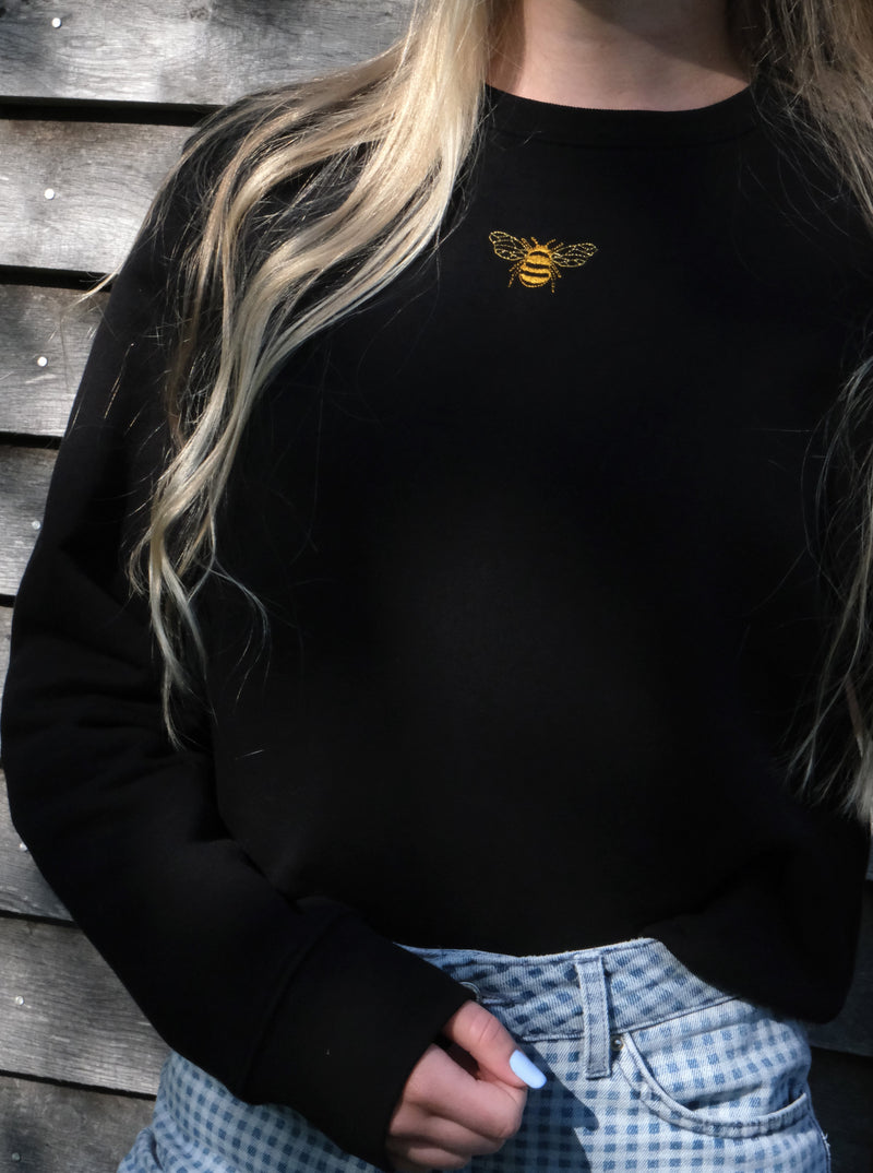 Embroidered golden bumble bee design modelled on a black sweatshirt. Styled with high waisted checkered jeans.