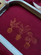 Embroidered golden house plant design on a burgundy sweatshirt within embroidery hoop.